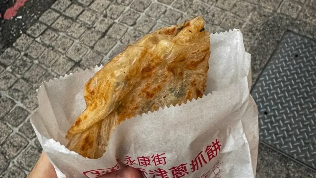 A golden, flaky Taiwanese scallion pancake with visible layers of dough and chopped scallion, fresh from the pan